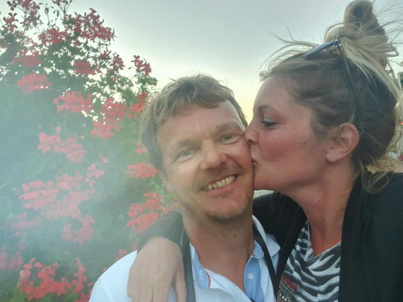 Evelien geeft Addy een kus voor een struik met rode bloemen