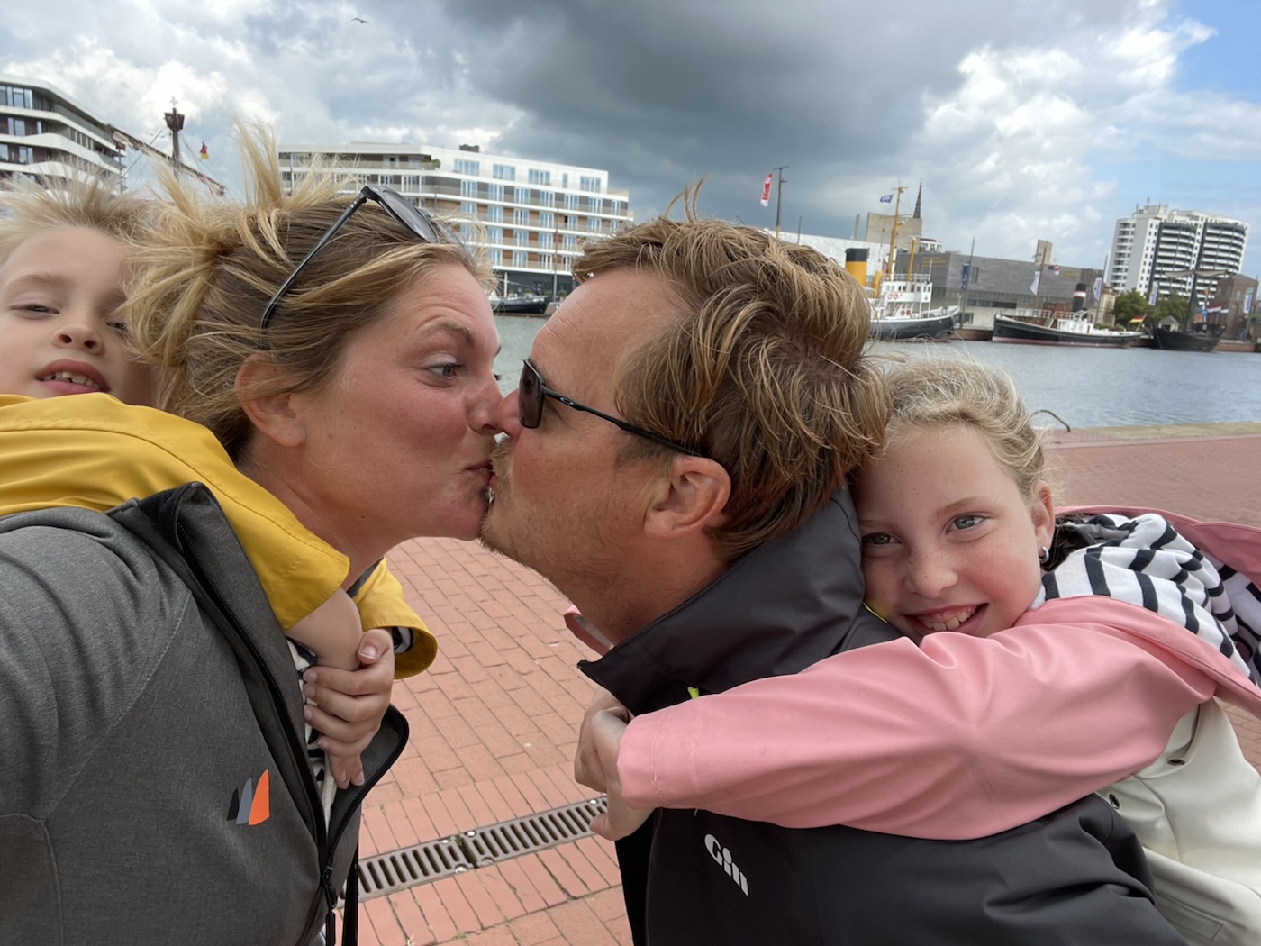 Addy en Evelien zoenen, met de kinderen op hun rug