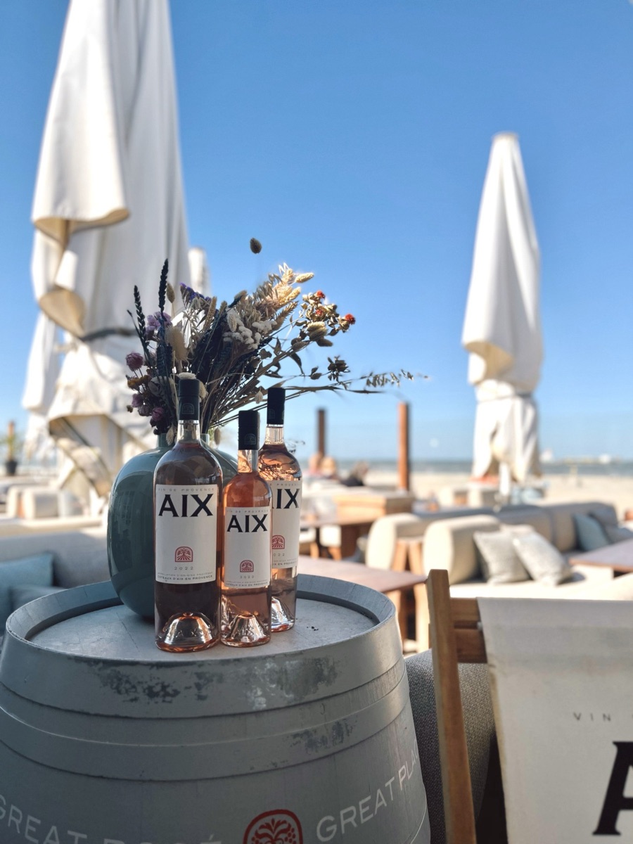 Flessen rosé op een ton op het terras van een strandpaviljoen, met parasols en zee op de achtergrond
